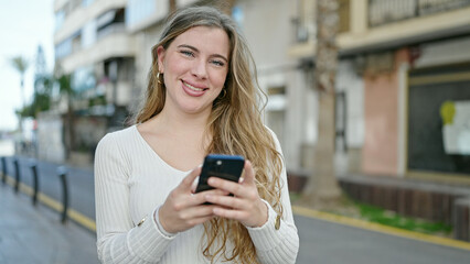 Young blonde woman smiling confident using smartphone at street