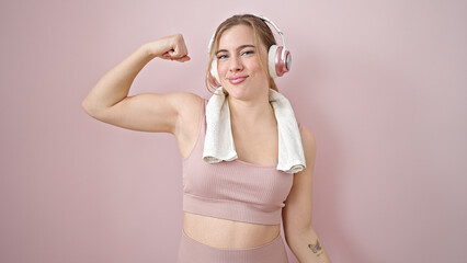 Young blonde woman listening to music doing strong gesture with arm over isolated pink background