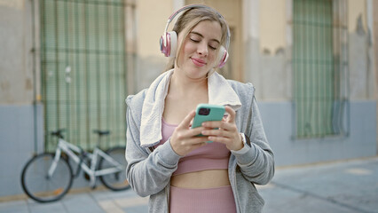Young blonde woman wearing sportswear listening to music at street