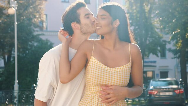 Smiling beautiful woman and her handsome boyfriend. Happy cheerful family. Couple posing in the street. Talking. Man kissing her gently at sunrise. During romantic date at sunny summer day