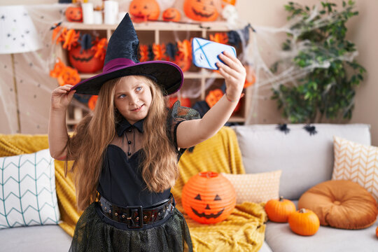 Adorable blonde girl wearing witch costume make selfie by smartphone at home