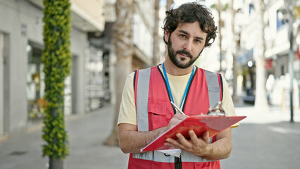 Young hispanic man having survey interview writing on clipboard at street