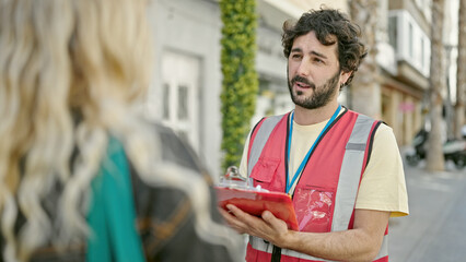 Young hispanic man having survey interview writing on clipboard at street
