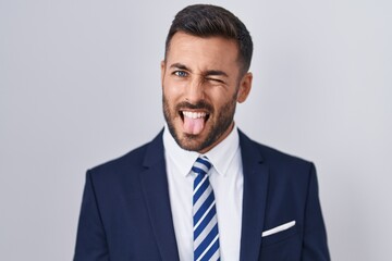 Handsome hispanic man wearing suit and tie sticking tongue out happy with funny expression. emotion concept.