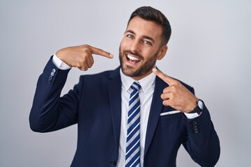 Handsome hispanic man wearing suit and tie smiling cheerful showing and pointing with fingers teeth and mouth. dental health concept.