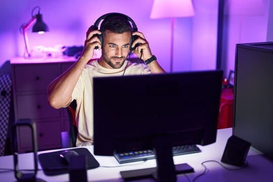 Young hispanic man streamer smiling confident sitting on table at gaming room