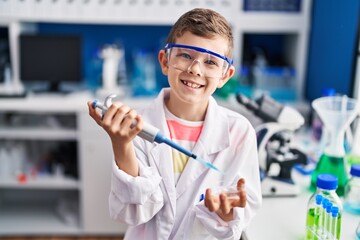 Blond child wearing scientist uniform using pipette at laboratory