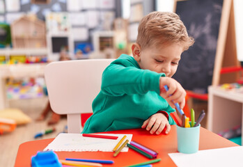 Adorable caucasian boy preschool student sitting on table drawing on notebook at kindergarten