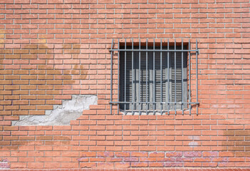 Rote verwitterte Backsteinwand mit vergittertem Fenster