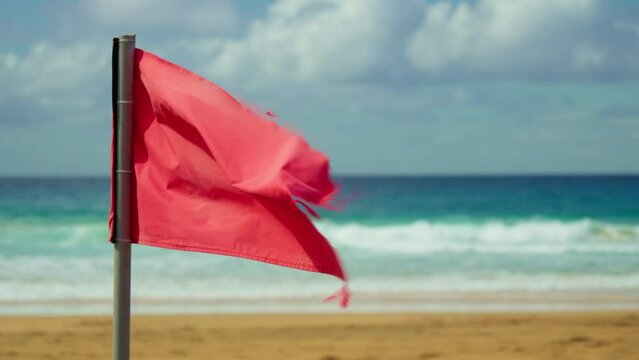 A red flag on the beach, waving in the wind.