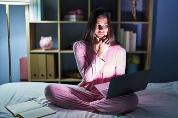 Young hispanic woman using computer laptop on the bed looking stressed and nervous with hands on mouth biting nails. anxiety problem.