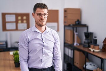 Young hispanic man at the office in shock face, looking skeptical and sarcastic, surprised with...