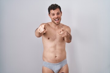 Fototapeta na wymiar Young hispanic man standing shirtless wearing underware pointing to you and the camera with fingers, smiling positive and cheerful