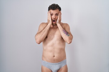 Fototapeta na wymiar Young hispanic man standing shirtless wearing underware afraid and shocked, surprise and amazed expression with hands on face