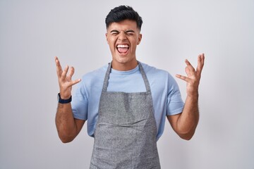 Hispanic young man wearing apron over white background celebrating mad and crazy for success with...