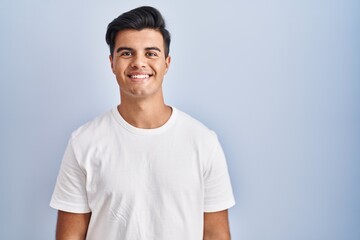 Hispanic man standing over blue background with a happy and cool smile on face. lucky person.