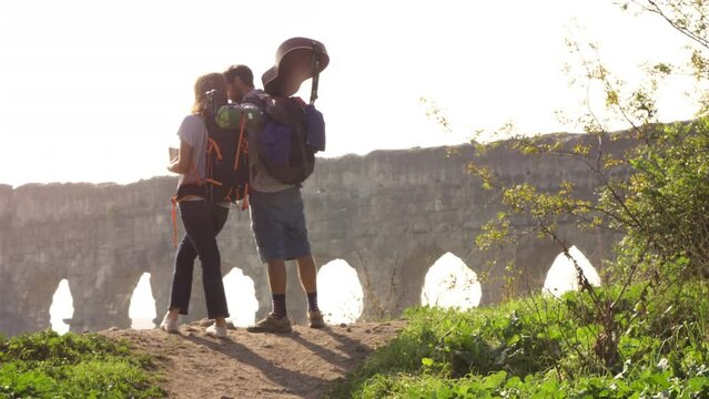 Young lovely couple backpackers tourists reading map pointing directions roman aqueduct arches in parco degli acquedotti park ruins in rome on romantic misty sunrise with guitar slow motion