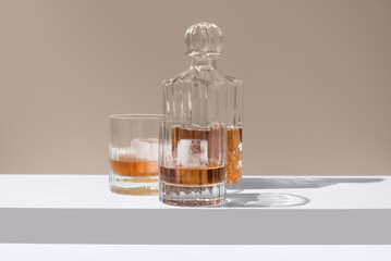 Dos vasos de whisky con hielo y decantador sobre un fondo beige