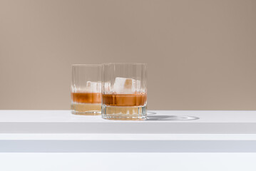 Dos vasos de whisky con hielo sobre un fondo beige