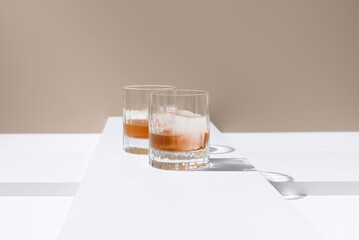 Dos vasos de whisky con hielo sobre un fondo beige