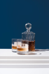 Dos vasos de whisky con hielo y decantador sobre un fondo azul