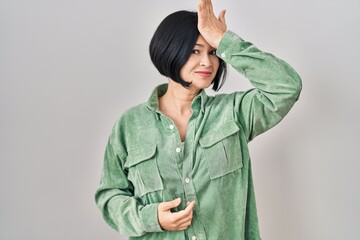 Young asian woman standing over white background surprised with hand on head for mistake, remember...