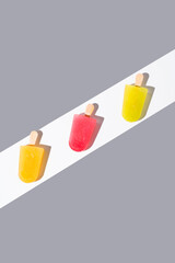 Paletas de hielo de colores. Palitos de helado naranja, rojo y amarillo sobre fondo gris. Concepto de verano. Vista superior	
