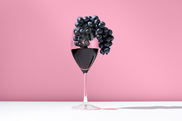 Copa de vino tinto con uvas negras sobre fondo rosa	