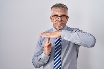 Hispanic business man with grey hair wearing glasses doing time out gesture with hands, frustrated...