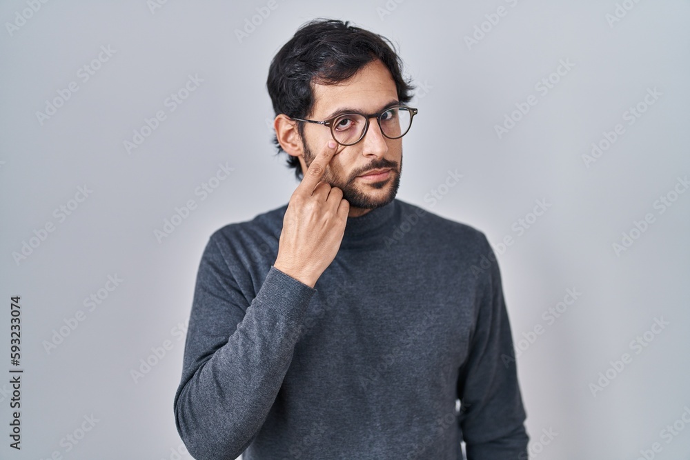 Poster handsome latin man standing over isolated background pointing to the eye watching you gesture, suspi