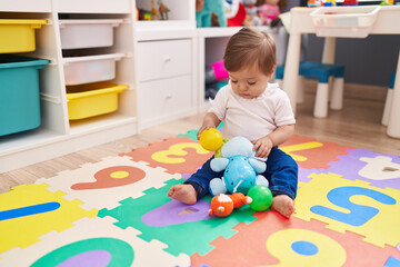 Adorable caucasian baby playing with ball and elephant toy sitting on floor at kindergarten