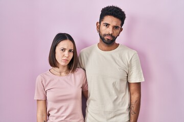 Obraz premium Young hispanic couple together over pink background skeptic and nervous, frowning upset because of problem. negative person.