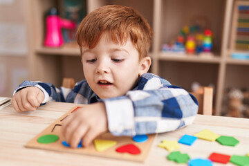 Adorable toddler playing with maths puzzle game sitting on table at classroom