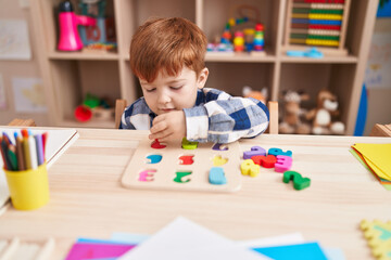Adorable toddler playing with maths puzzle game sitting on table at classroom