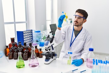 Young hispanic man wearing scientist uniform holding test tube at laboratory