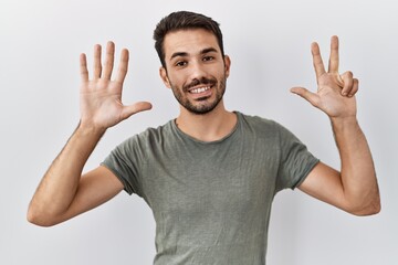 Fototapeta premium Young hispanic man with beard wearing casual t shirt over white background showing and pointing up with fingers number eight while smiling confident and happy.