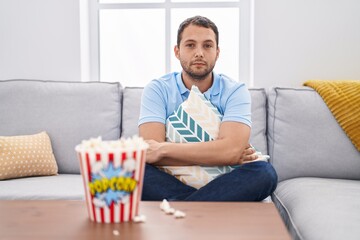 Hispanic man watching tv at home sitting on the sofa relaxed with serious expression on face. simple and natural looking at the camera.