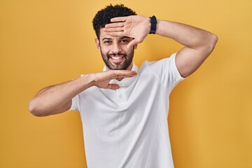 Fototapeta na wymiar Arab man standing over yellow background smiling cheerful playing peek a boo with hands showing face. surprised and exited