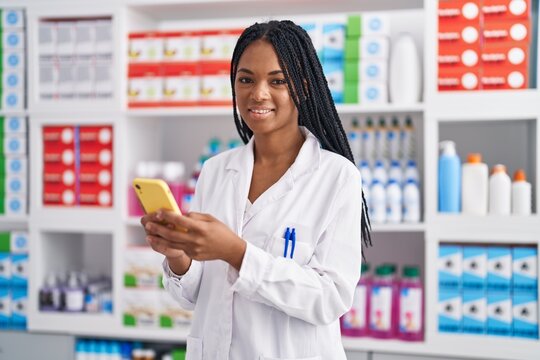 African american woman pharmacist smiling confident using smartphone at pharmacy
