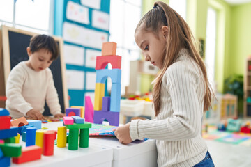 Adorable boy and girl playing with construction blocks and vocabulary puzzle at kindergarten