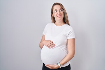 Young pregnant woman expecting a baby, touching pregnant belly smiling looking to the side and...