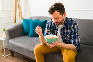 Happy man eating cereal for breakfast on the sofa