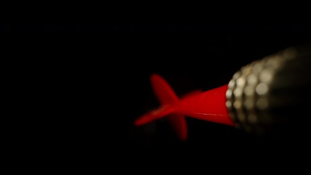 A red dart for playing darts rotates and flies on a black background to meet the camera, extremely close-up. Slow motion.