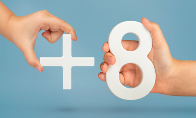 The number eight and the plus symbol in the hands of a child on a blue background. White number 8...
