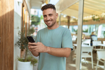 Young hispanic man smiling confident using smartphone at coffee shop terrace