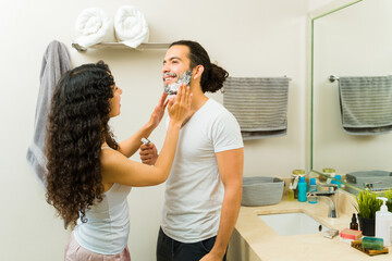 Smiling woman shaving the beard of a young man
