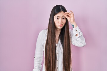 Chinese young woman standing over pink background worried and stressed about a problem with hand on forehead, nervous and anxious for crisis