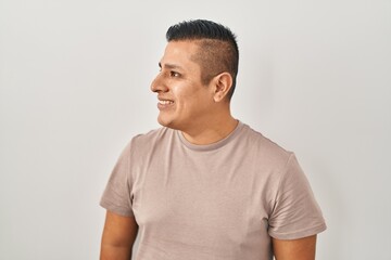 Hispanic young man standing over white background looking away to side with smile on face, natural expression. laughing confident.