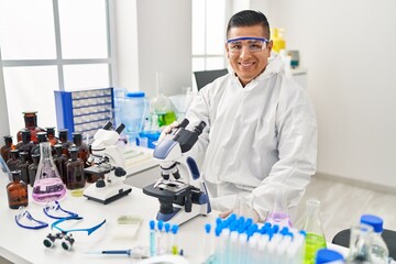 Young latin man scientist wearing covid protection uniform using microscope at laboratory