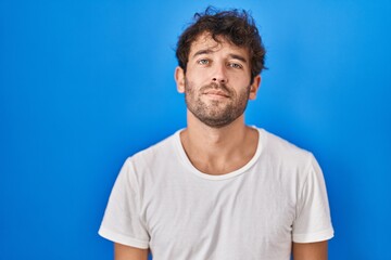 Fototapeta premium Hispanic young man standing over blue background relaxed with serious expression on face. simple and natural looking at the camera.